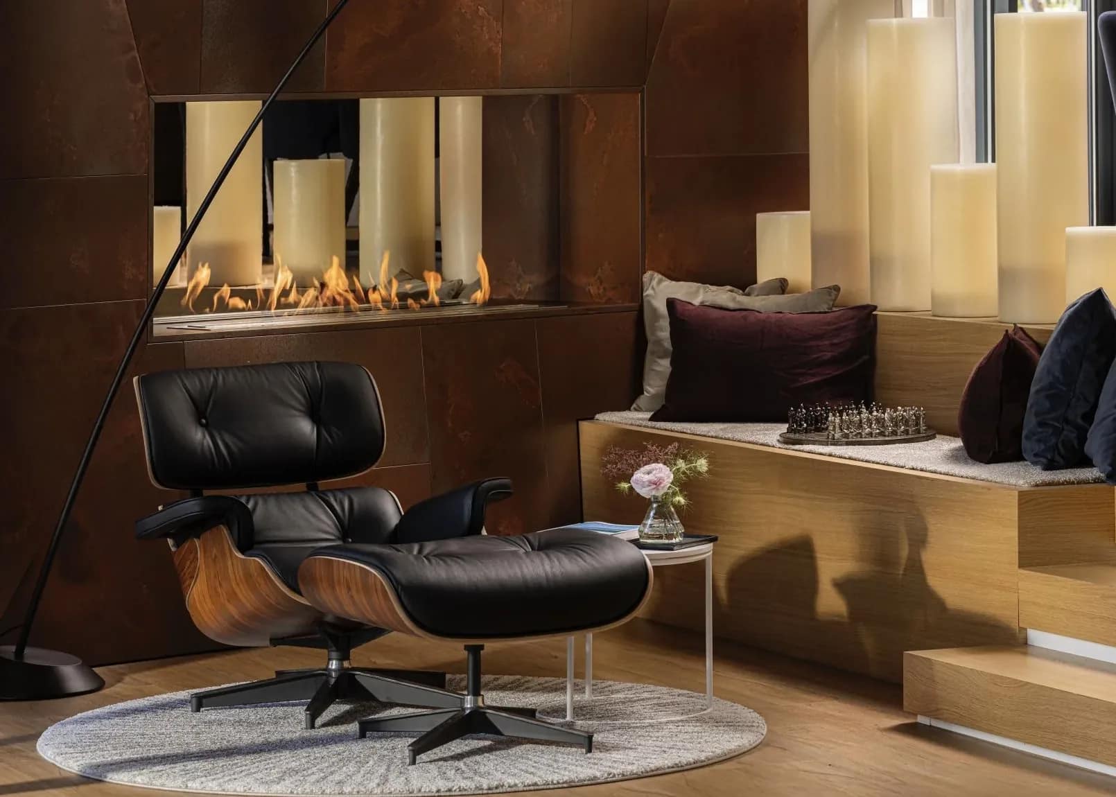 The Eames chair drawn up to the fire, pillar candles along the hearth