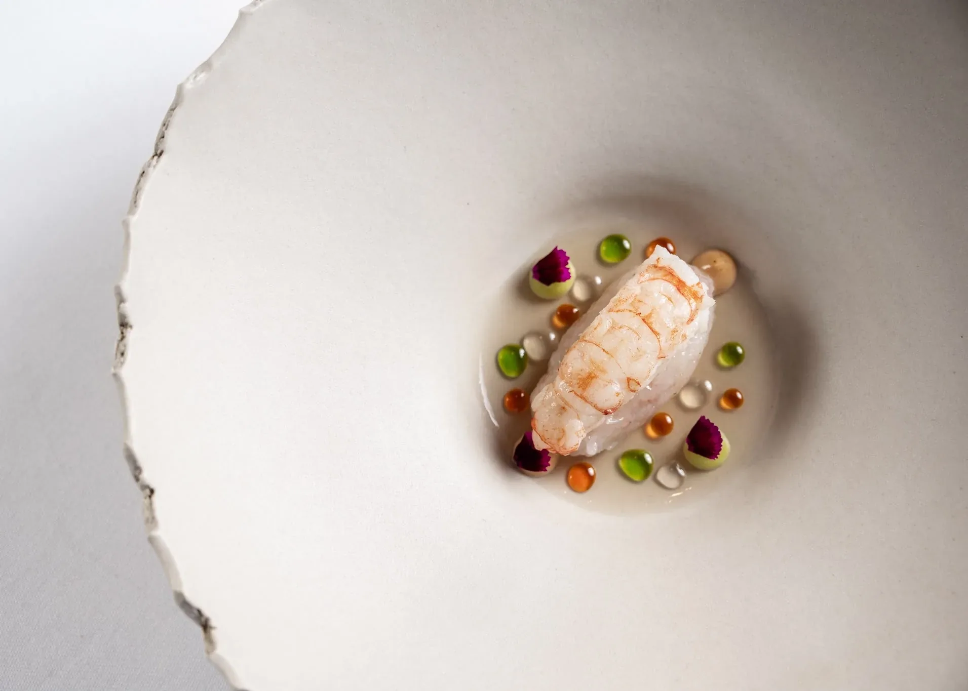 A langoustine plated with pearls of sauce and petals
