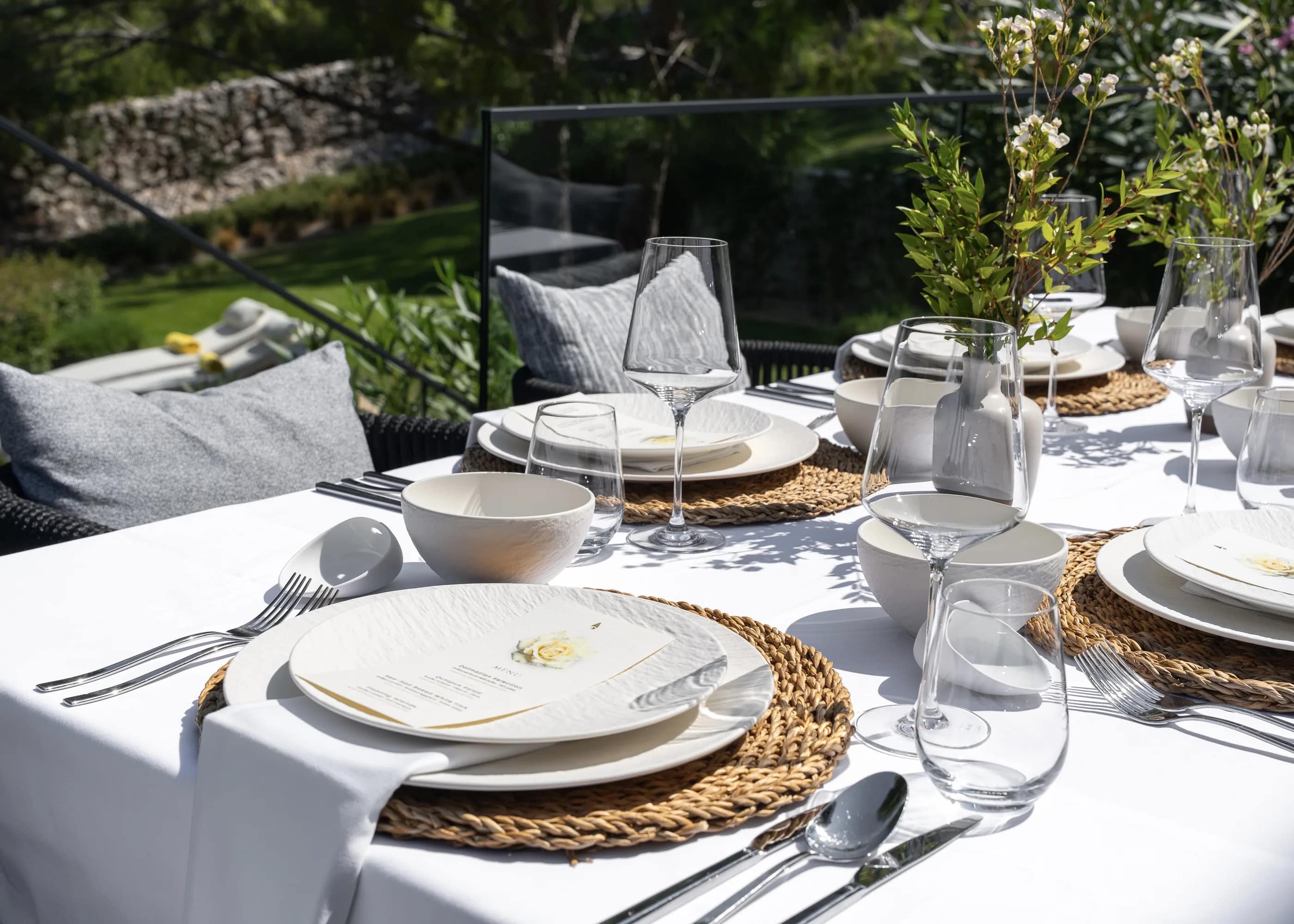 The outdoor table laid on woven mats, the cove beyond