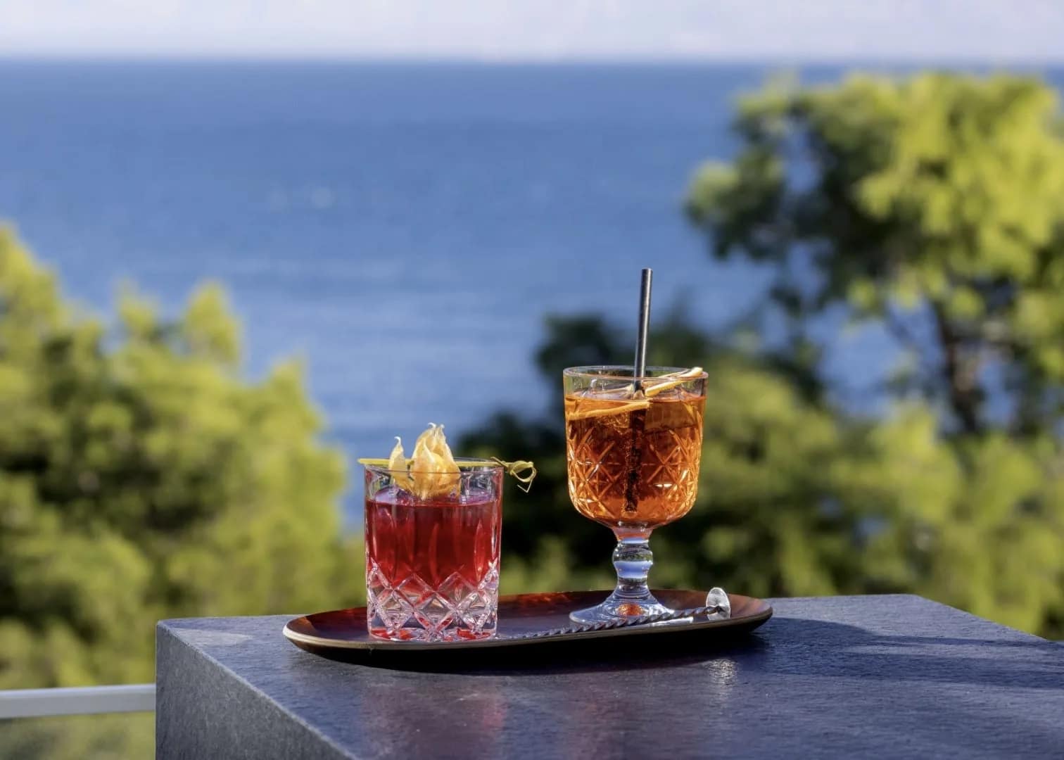 Two cocktails on a tray, above the sea and the pines