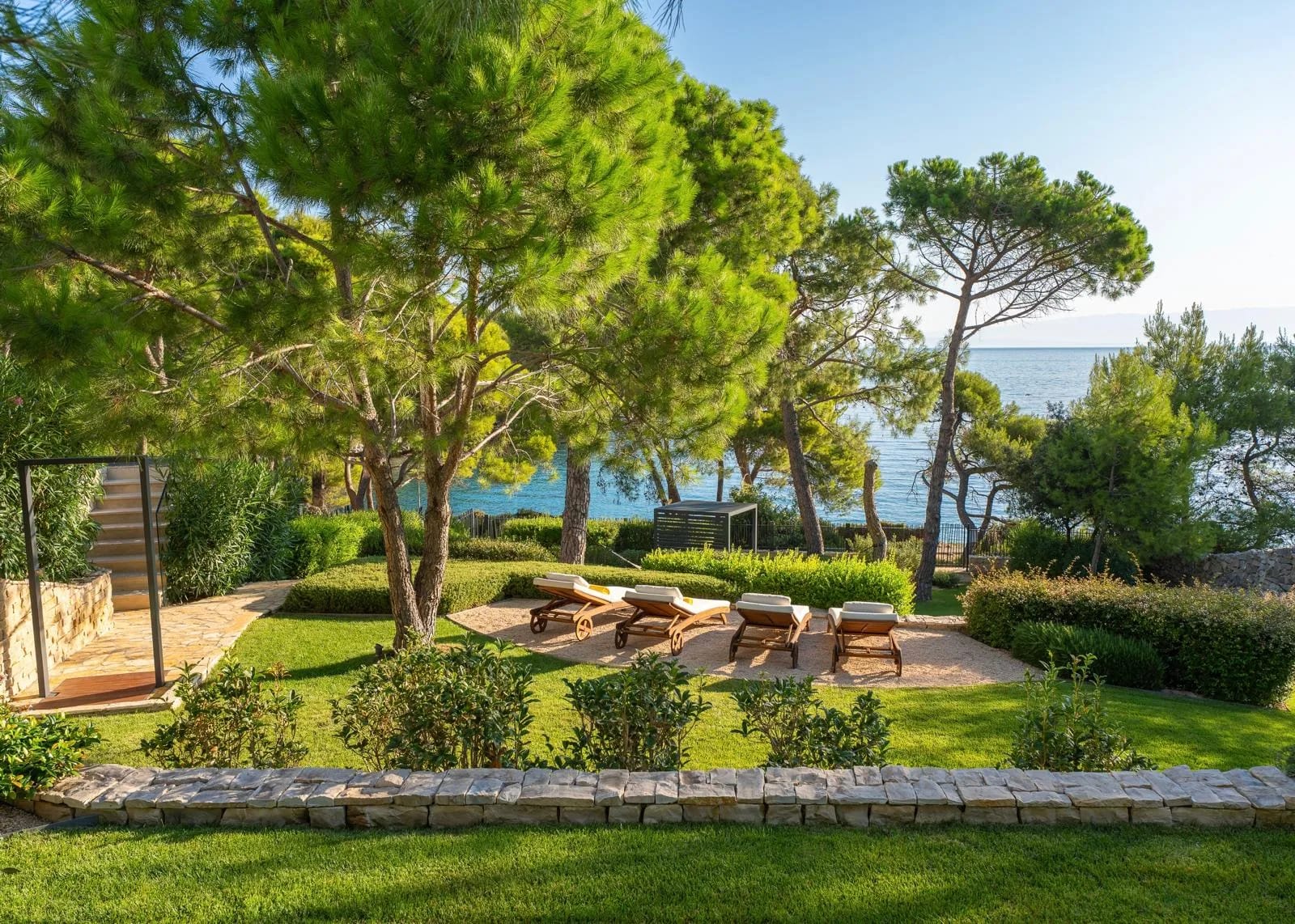 Loungers on the manicured lawn among the pines, the sea beyond