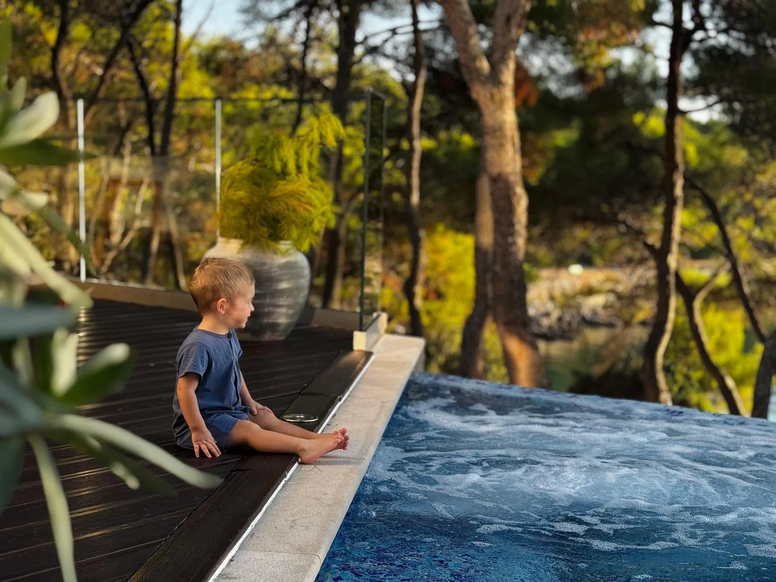 A child sitting at the edge of the heated infinity pool, feet in the water, watching the pines