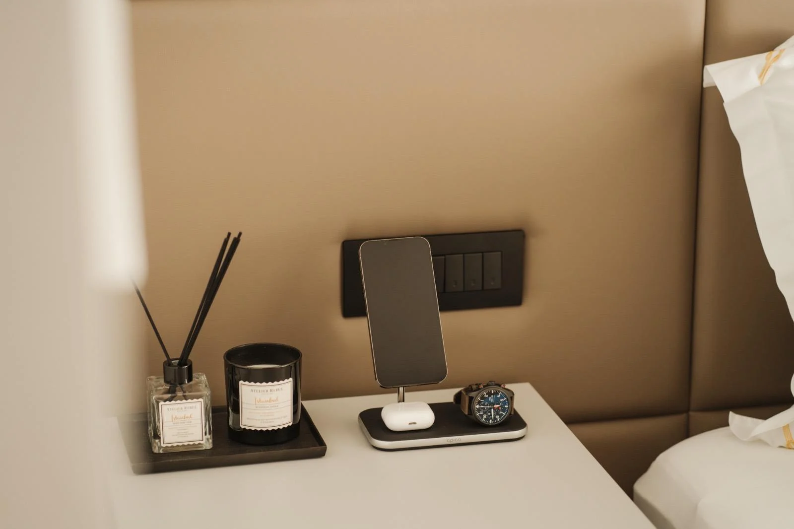 Ambroz bedside — the Atelier Rebul candle and diffuser, a watch and phone on the charging tray
