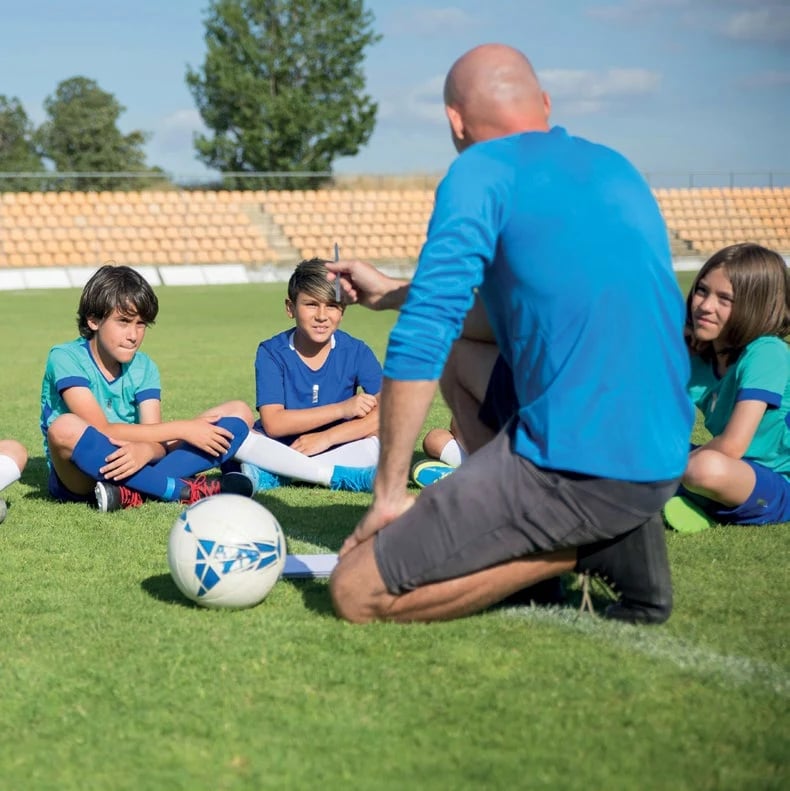 A football coach instructing young players on the pitch