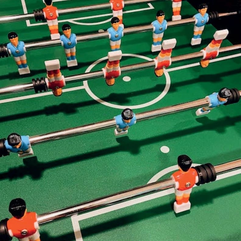 A top-down view of a foosball table with blue and orange players