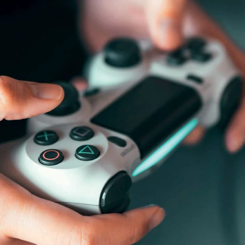 Hands holding a glowing PlayStation controller in low light