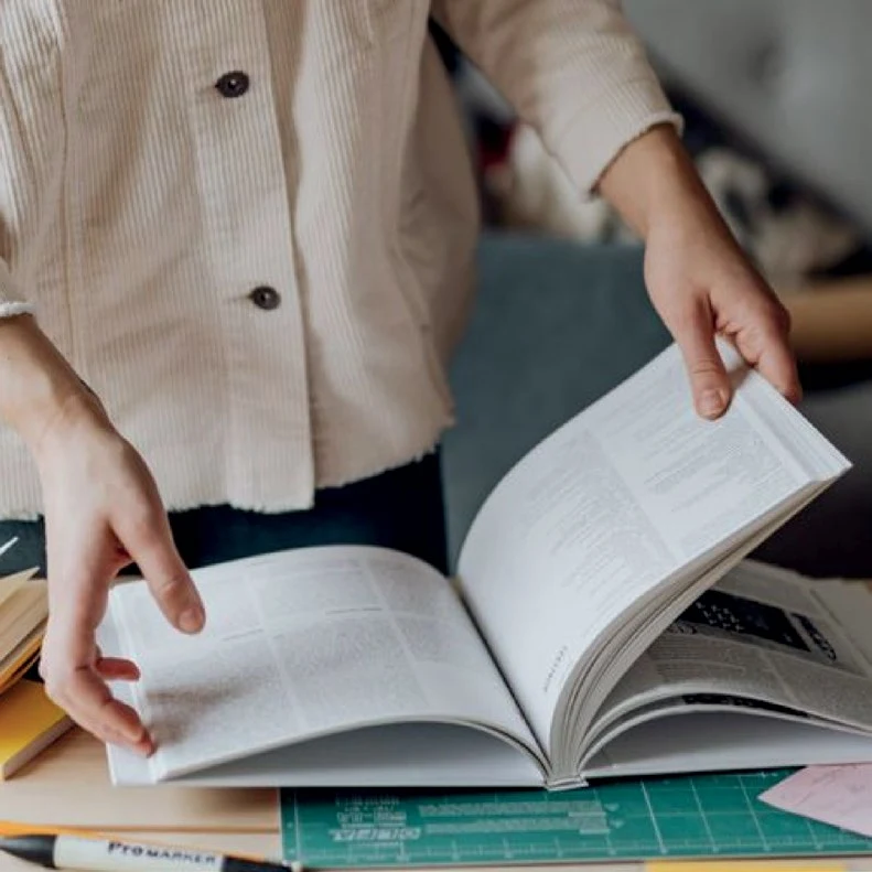 Hands holding an open textbook at a study desk