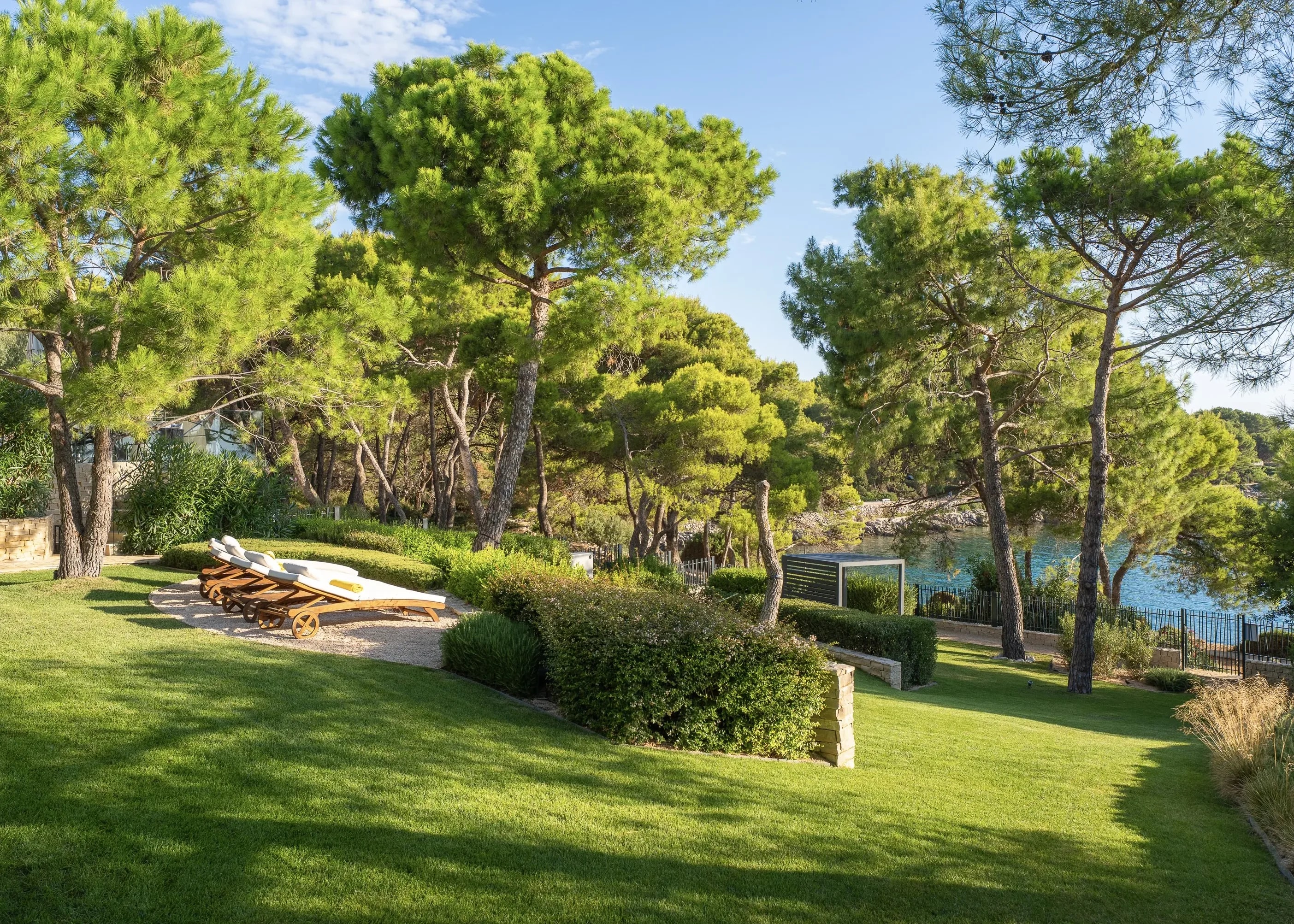 The villa garden — a quiet lawn with loungers tucked among the pines, by the cove