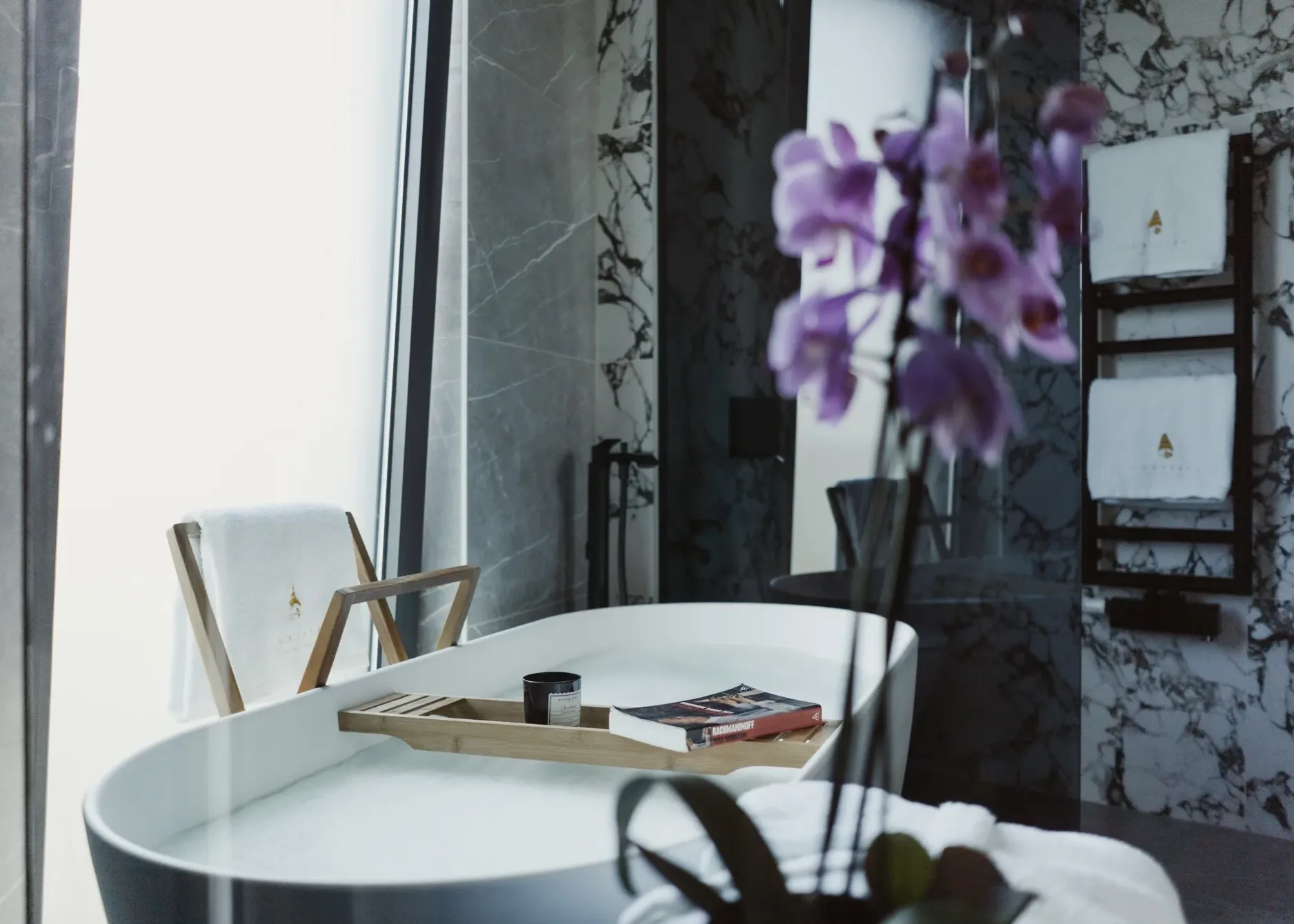 Aldebrand bathroom — freestanding marble tub with orchid bouquet and reading tray