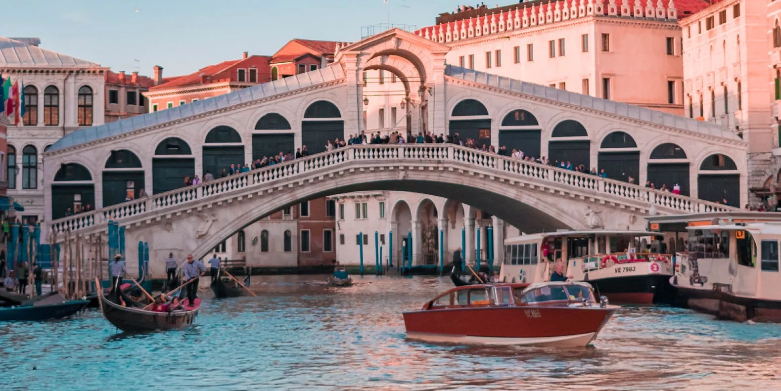 The Rialto Bridge in Venice at sunset, gondolas and water taxis on the Grand Canal