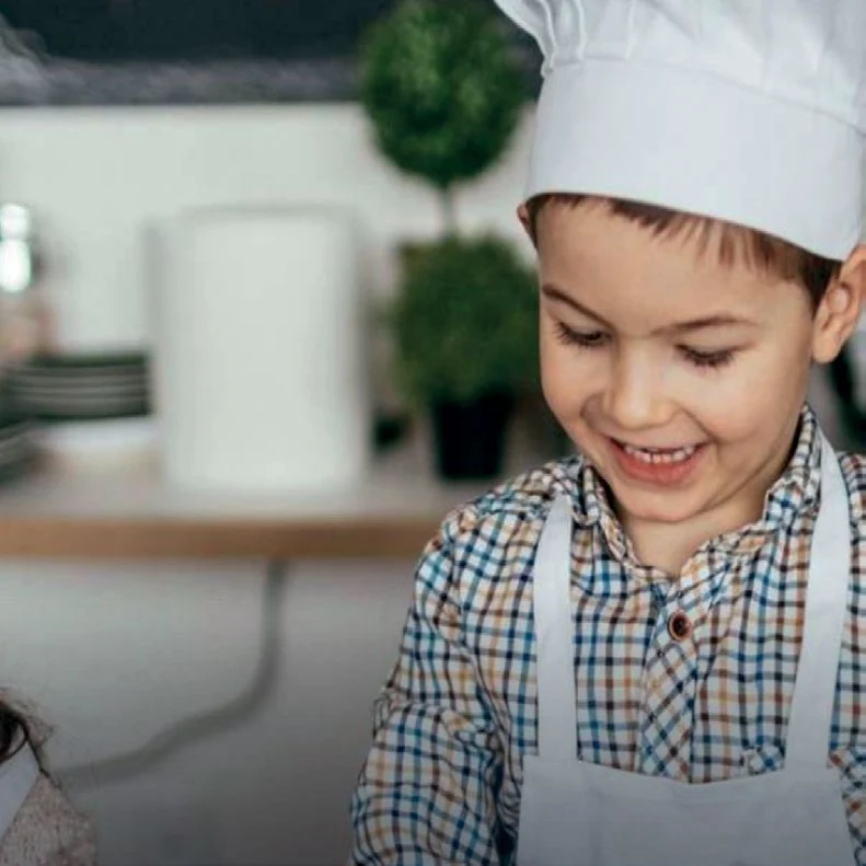 A young boy smiling in a chef's hat at the villa kitchen