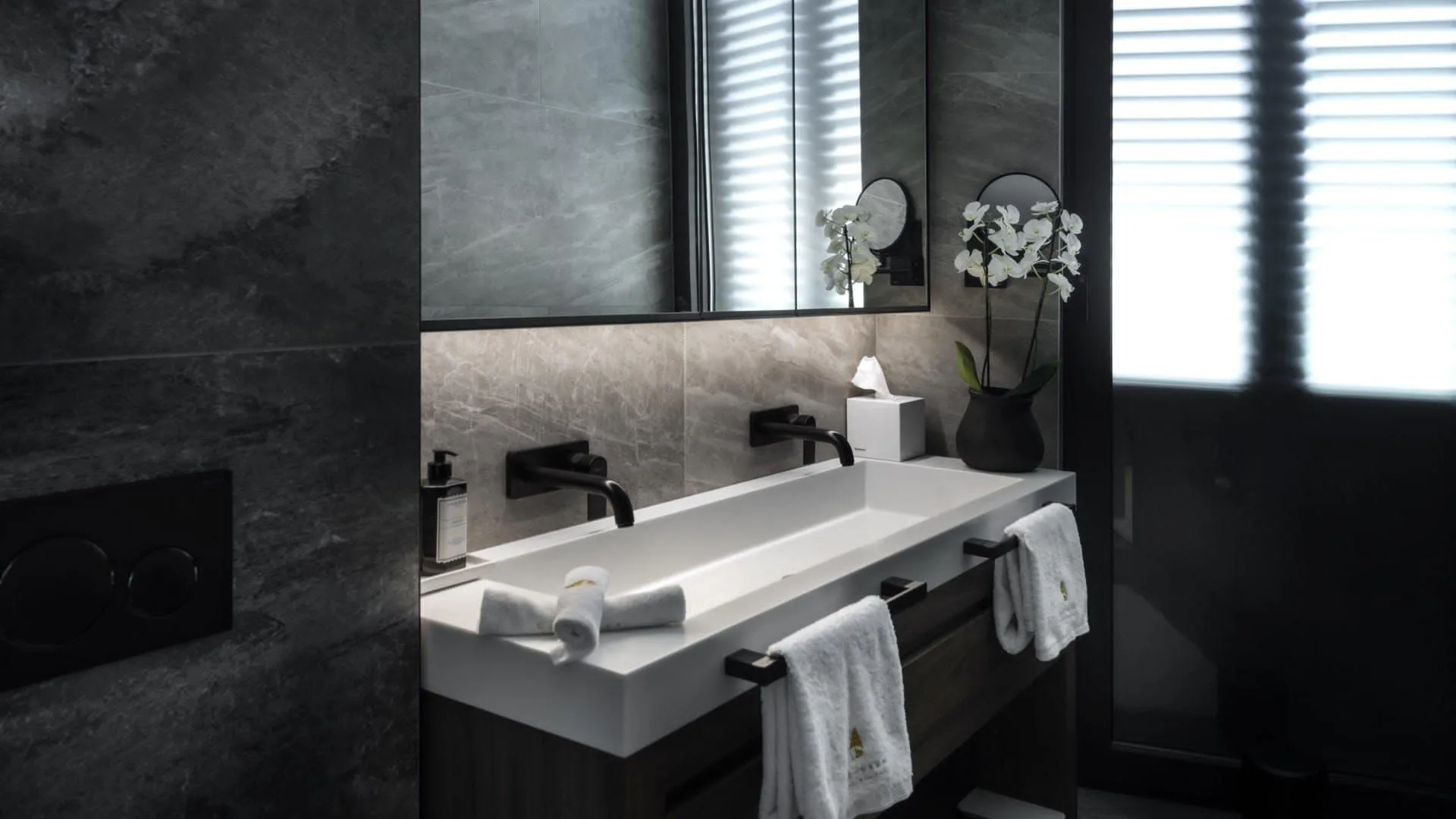 Spiridon bathroom — the long double basin with black fixtures and an orchid