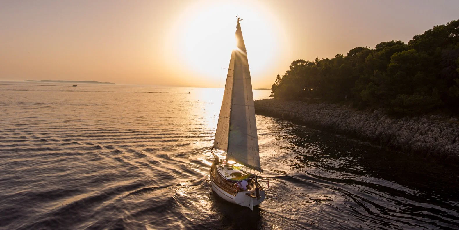 A sailing cutter heading into the sun, the sail glowing against a golden sky