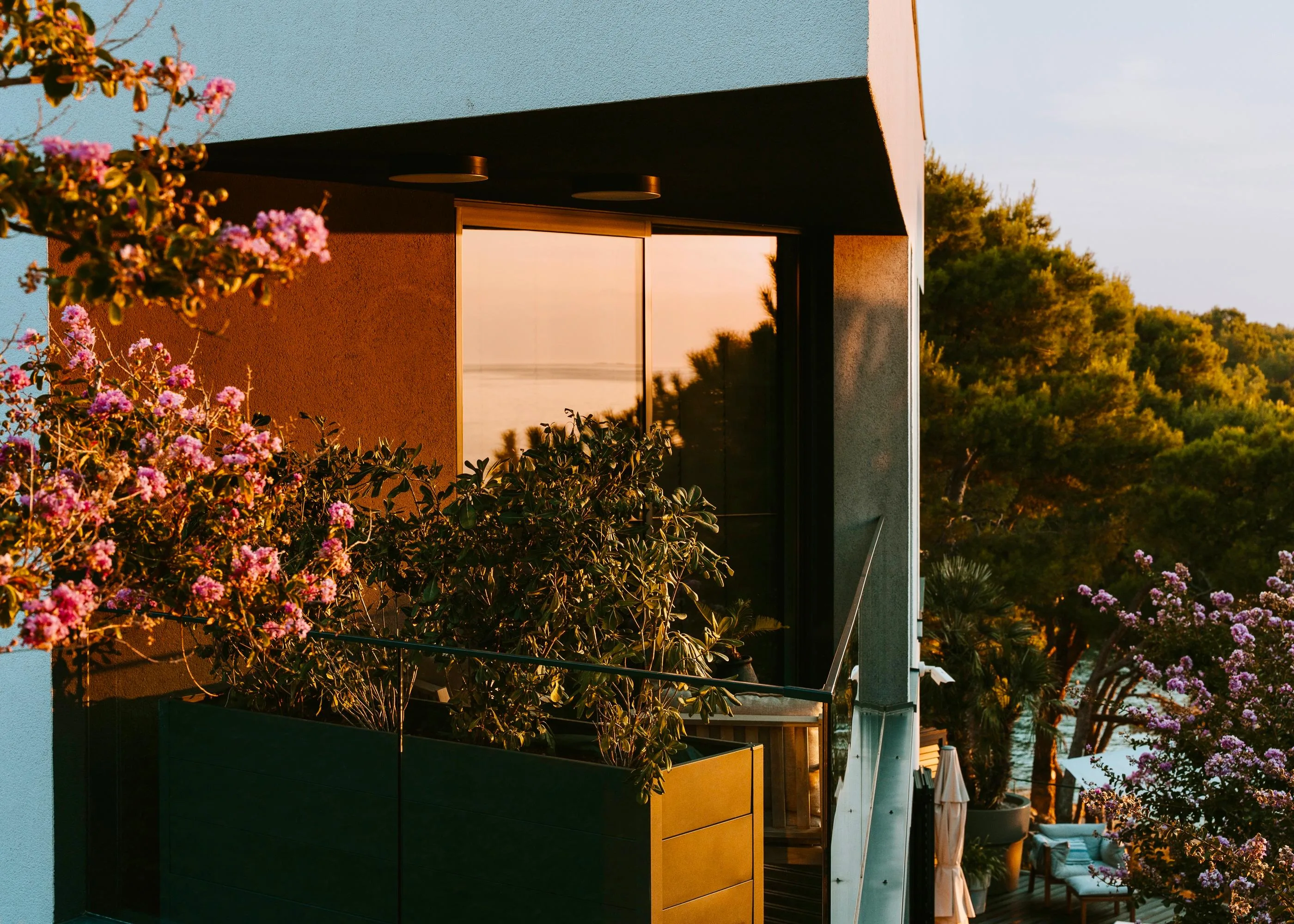 The Tesla suite's terrace at sunset — crape myrtle in bloom, the sea held in the glass
