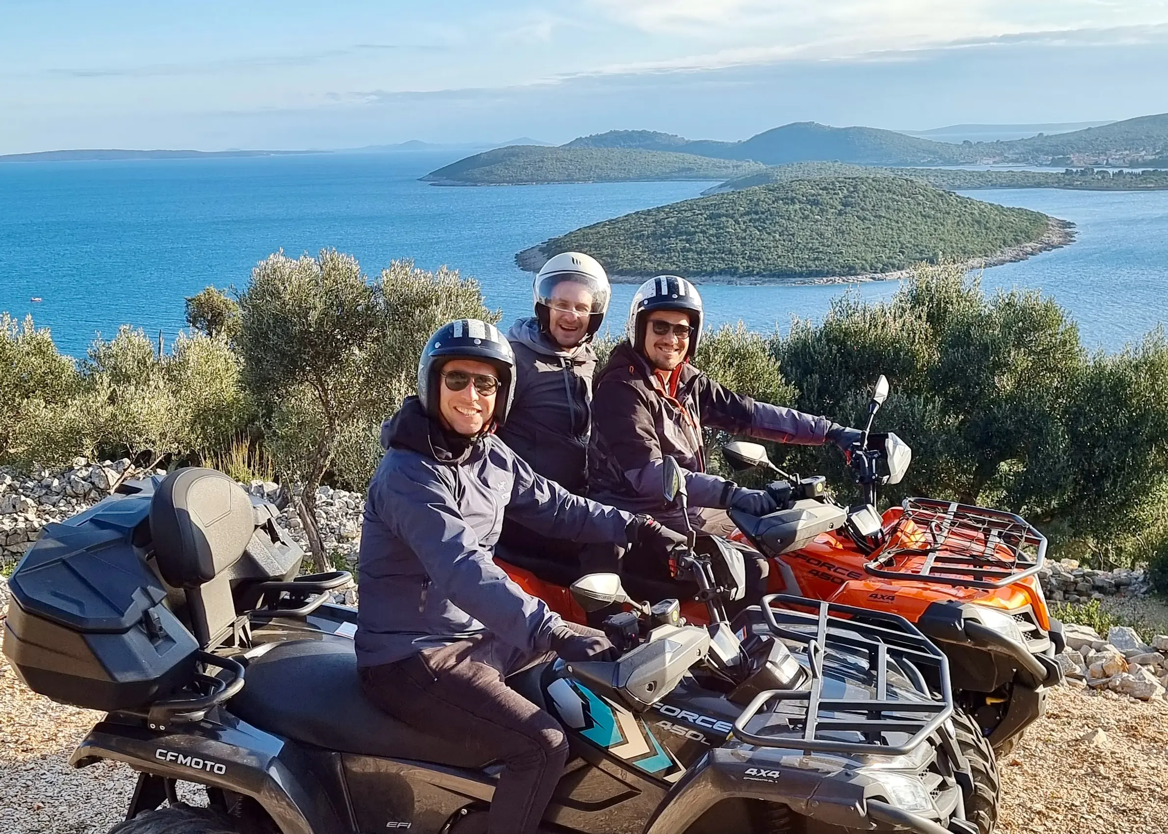 Three guests on quads paused on the ridge, the islands and the bay behind them