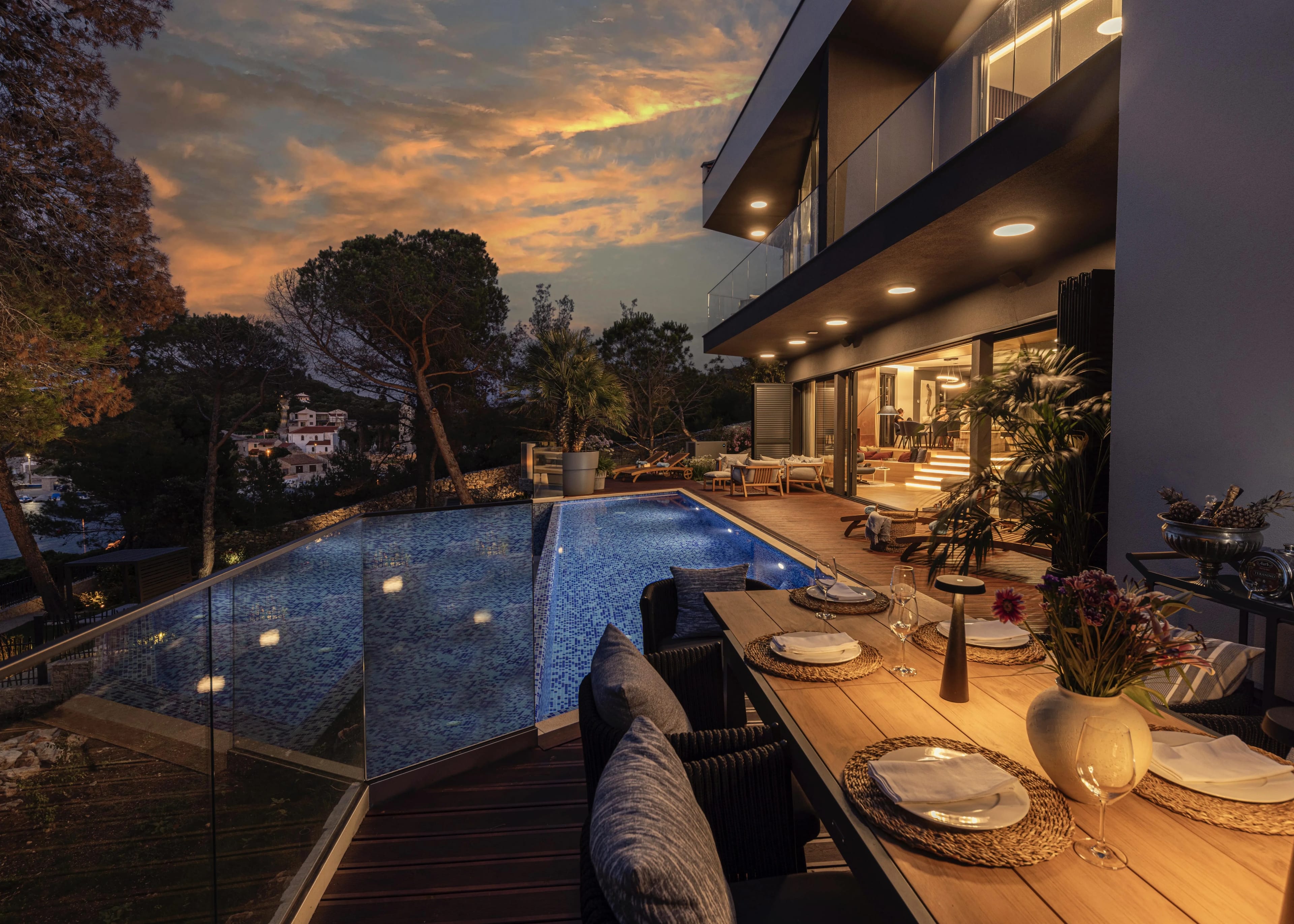 The terrace set for dinner in the evening, the lit pool and lounge beyond