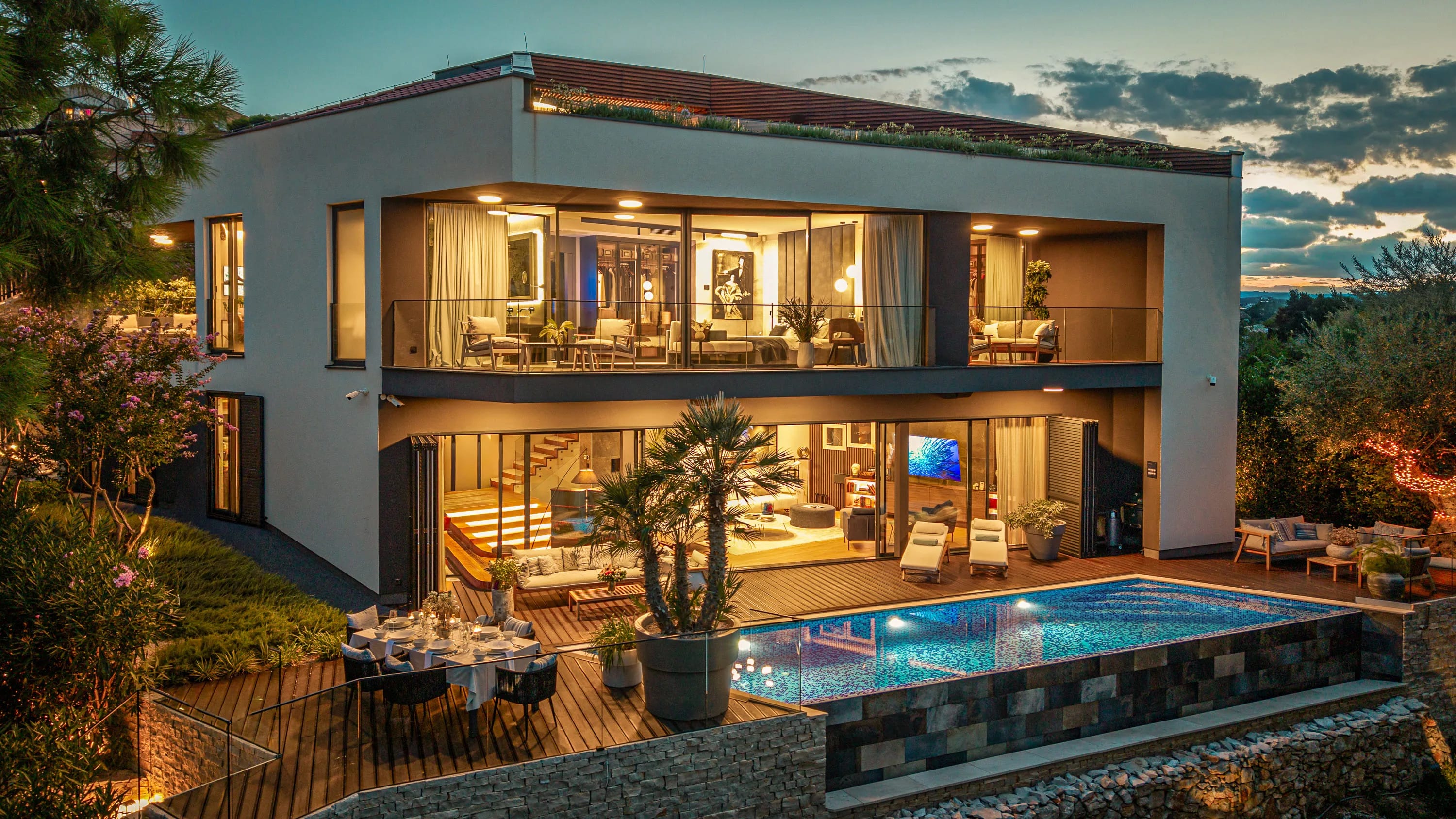 The villa lit from within at twilight, the pool and dining deck below