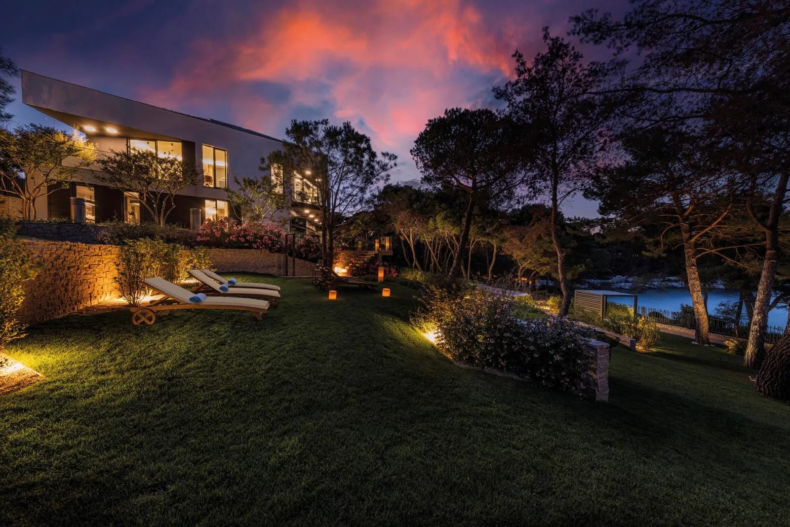 Loungers on the lawn under a pink dusk sky, the villa lit behind